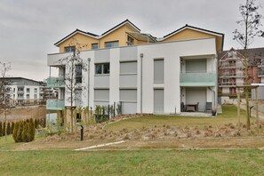 Ein modernes, mehrgeschossiges Wohngebäude mit Flachdach, großen Fenstern und einer kleinen Außen-Sitzgelegenheit.