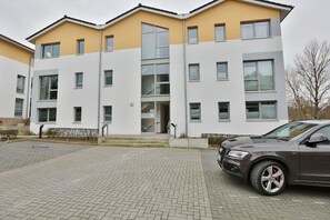 Un immeuble moderne à plusieurs étages, doté d’une façade jaune et blanche, de grandes fenêtres et d’un espace d’entrée pavé.