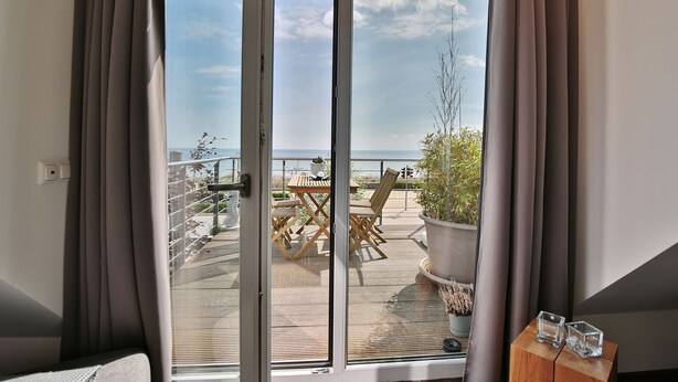 A balcony with a table and chairs, a potted plant, and a view of the sea.