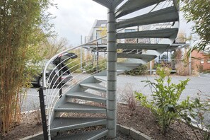 En spiraltrappe med gelændere i metal, omgivet af planter og en parkeret bil.
