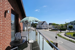 A balcony with a table and chairs, a striped umbrella, and a view of a residential street.