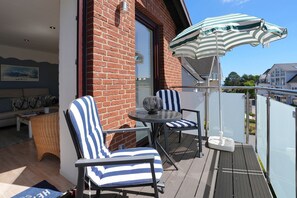 Ein Balkon mit zwei gestreiften Stühlen, einem Tisch und einem gestreiften Sonnenschirm.