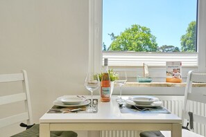 A dining table with plates, glasses, and a bottle, set against a window with a view of trees and a book titled 'TRÜBSTÜCK TO GO'.