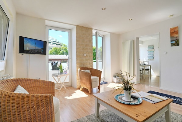 A modern living room with a television, wicker furniture, a wooden coffee table, and a view through the glass door.