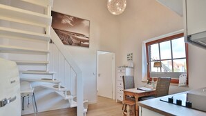 Una cocina moderna con una mesa y sillas de madera, un refrigerador blanco, y una escalera que conduce a otro nivel.