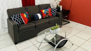 A living room with a black sofa, a glass coffee table, a red wall, and a ceiling fan. - 5** Start New Beautiful Aparment w/ 2 Bedrooms. (San Juan)