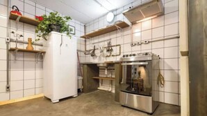 Eine Küche mit weiß gefliesten Wänden, einem Kühlschrank, einem Backofen und einem Spülbecken.