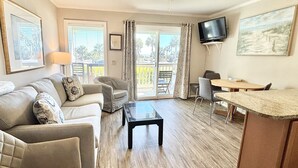 Uma sala de estar com sofá, poltronas, mesa de centro, televisão e um espaço de jantar com mesa e cadeiras.