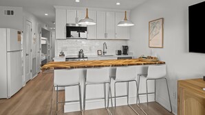 A modern kitchen with white cabinetry, a wooden island with bar stools, a built-in oven, and pendant lighting.