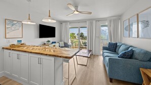 A modern kitchen with white cabinets, a wooden countertop, and pendant lights. There is a dining area with a blue sofa and a table.
