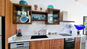 A modern kitchen with wooden cabinets, a built-in oven, and a glass-fronted shelving unit displaying dishes and utensils. - Unit 216-Casa Ricardo-Ocean View RENOVATED!! (Cabo San Lucas)