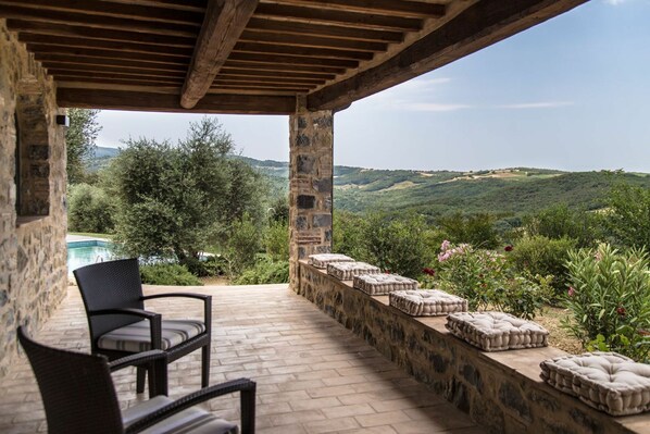 Un patio cubierto con muros de piedra, una piscina y vistas a colinas ondulantes.