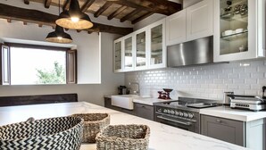 A modern kitchen with white cabinets, a stainless steel range, and a marble countertop. There are wicker baskets on the counter and a window providing natural light.