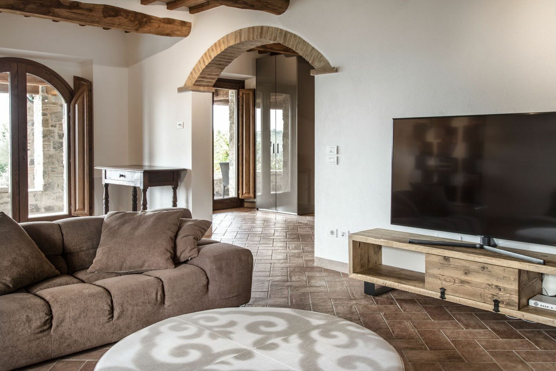 Ein Wohnzimmer mit einer Couch, einem Hocker und einem Fernseher auf einem Holzboden.