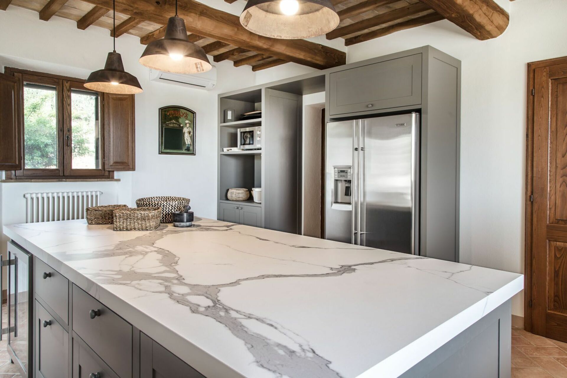 A kitchen with a marble island, stainless steel appliances, wooden beams, and pendant lighting.