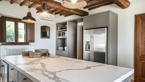 A kitchen with a marble island, stainless steel appliances, wooden beams, and pendant lighting.