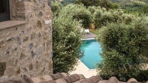 A stone building with a view of a swimming pool surrounded by olive trees.
