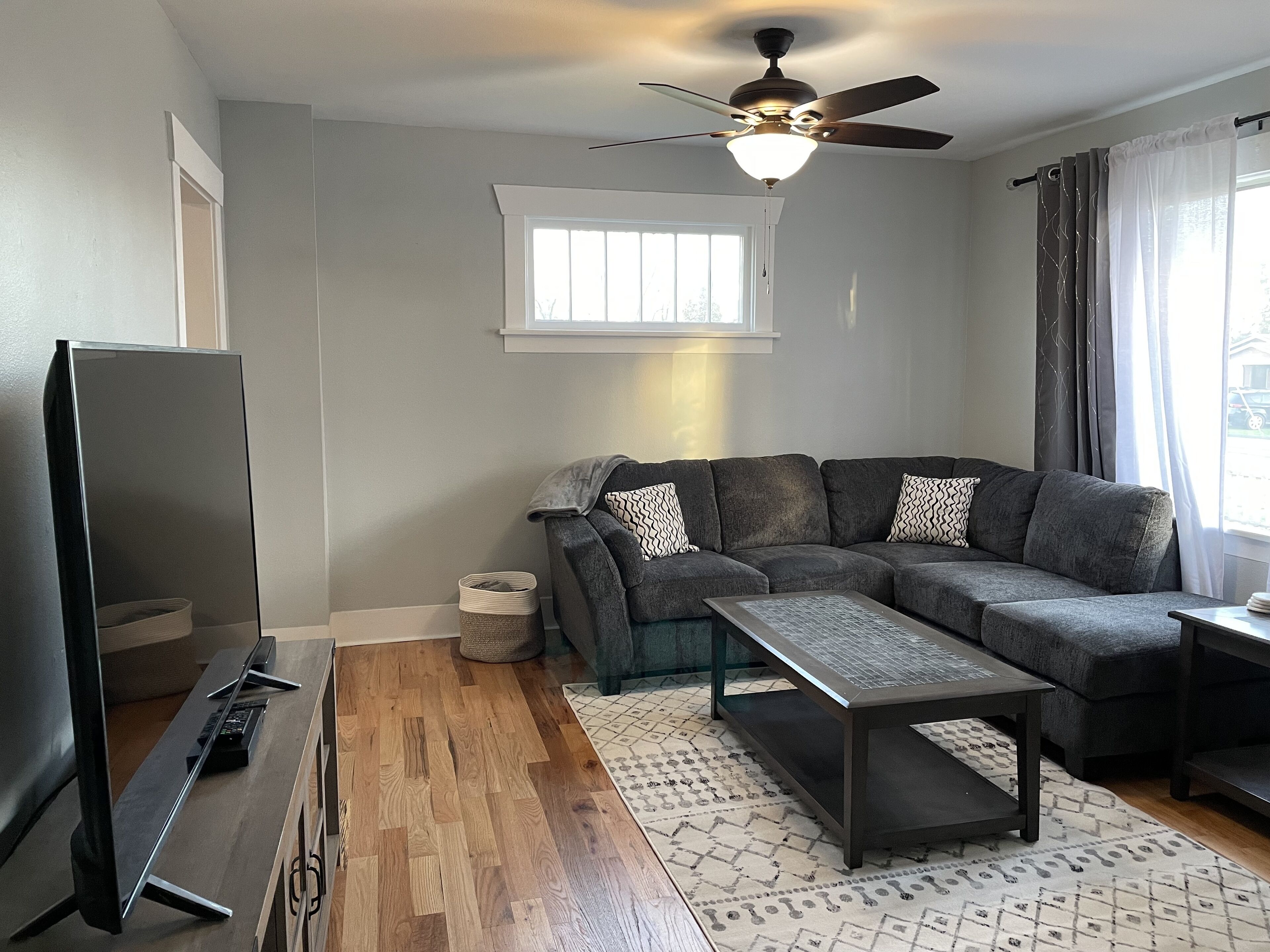 A living room with a grey sofa, a coffee table, a TV, and a ceiling fan.