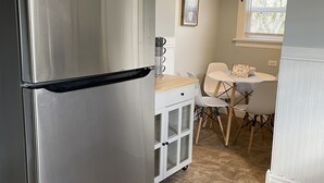 A kitchen with a stainless steel refrigerator, a small table with chairs, and a window with blinds.
