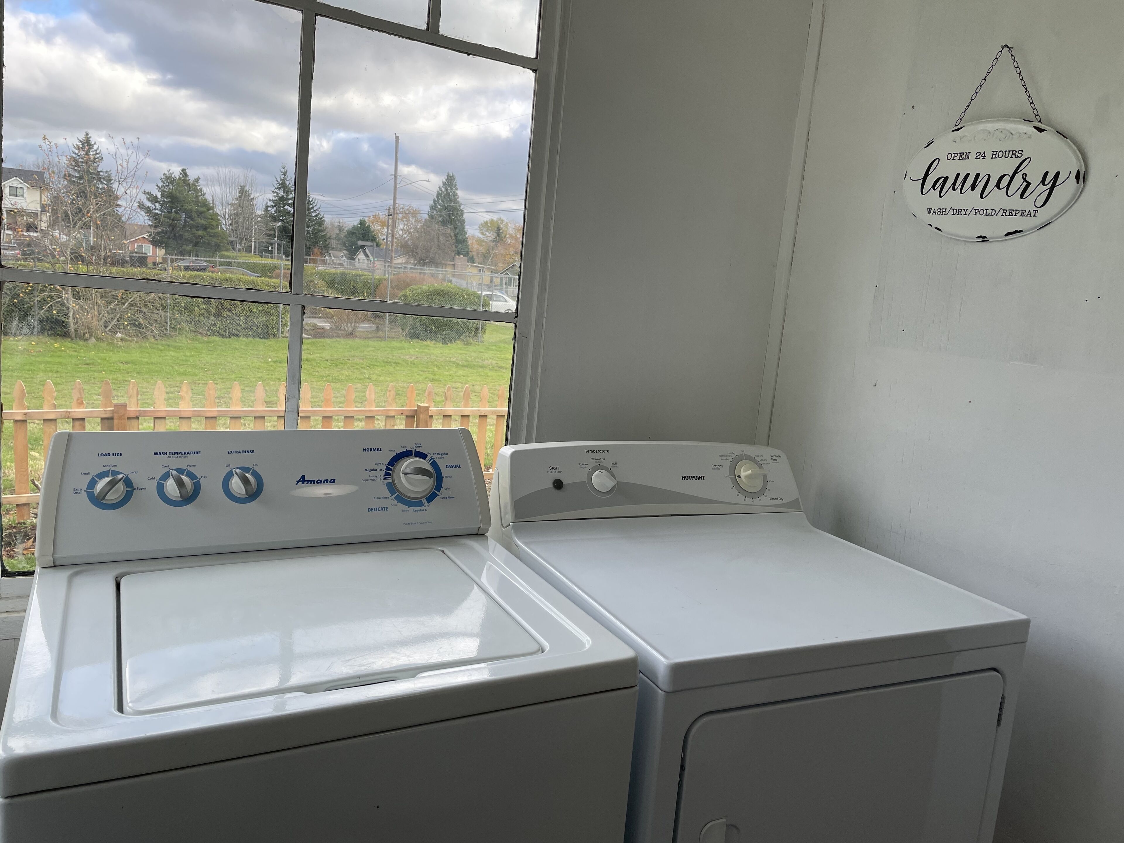 Een wasmachine en droger met voorlader in een wasserij met uitzicht op een woongebied door een raam.