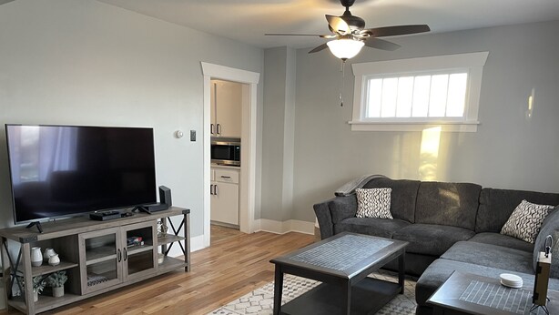 A modern living room with a flat-screen TV, a gray sofa, a coffee table, and a ceiling fan.