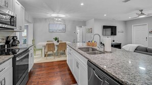 A modern kitchen with granite countertops, stainless steel appliances, and a dining area with wicker chairs.