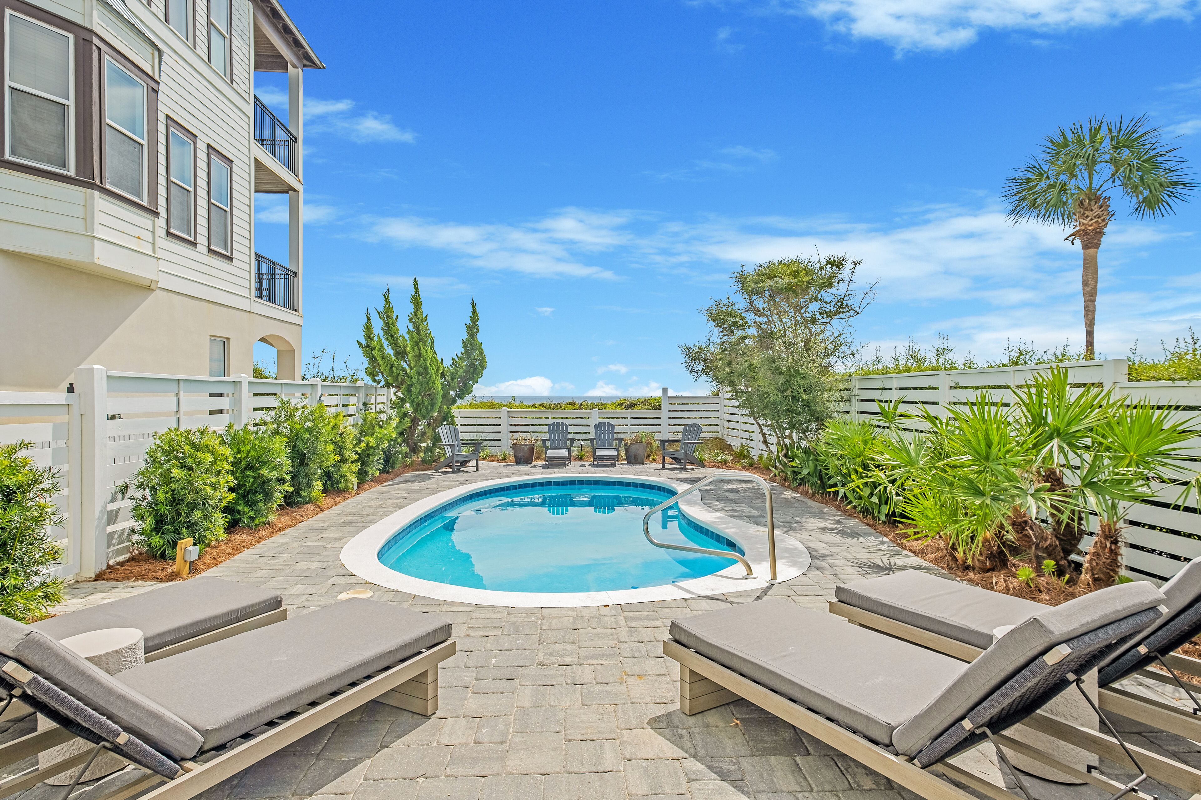 A swimming pool with lounge chairs, surrounded by greenery and a building with balconies.