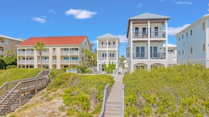 Un hôtel situé sur la côte, doté de nombreux balcons, d’une promenade en bois et d’une végétation luxuriante en bord de mer.