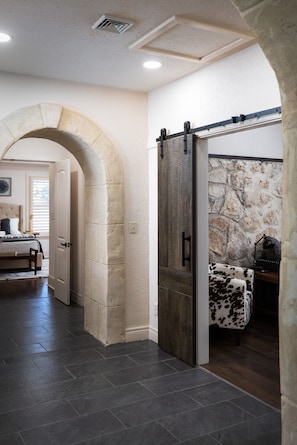 A hallway with a stone archway leading to a bedroom with a bed and a nightstand.