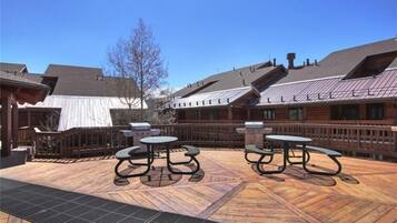 Een terras buiten met picknicktafels en barbecuegrills.