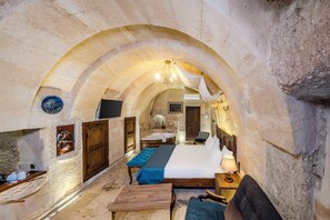 A stone-walled room with a bed, a wooden bench, a small table, a chair, and a bathtub. - Pegas Cave Suites (Ürgüp)