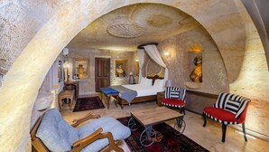 A room with a bed, a desk, a chair, a sofa, and a wheelchair. - Pegas Cave Suites (Ürgüp)