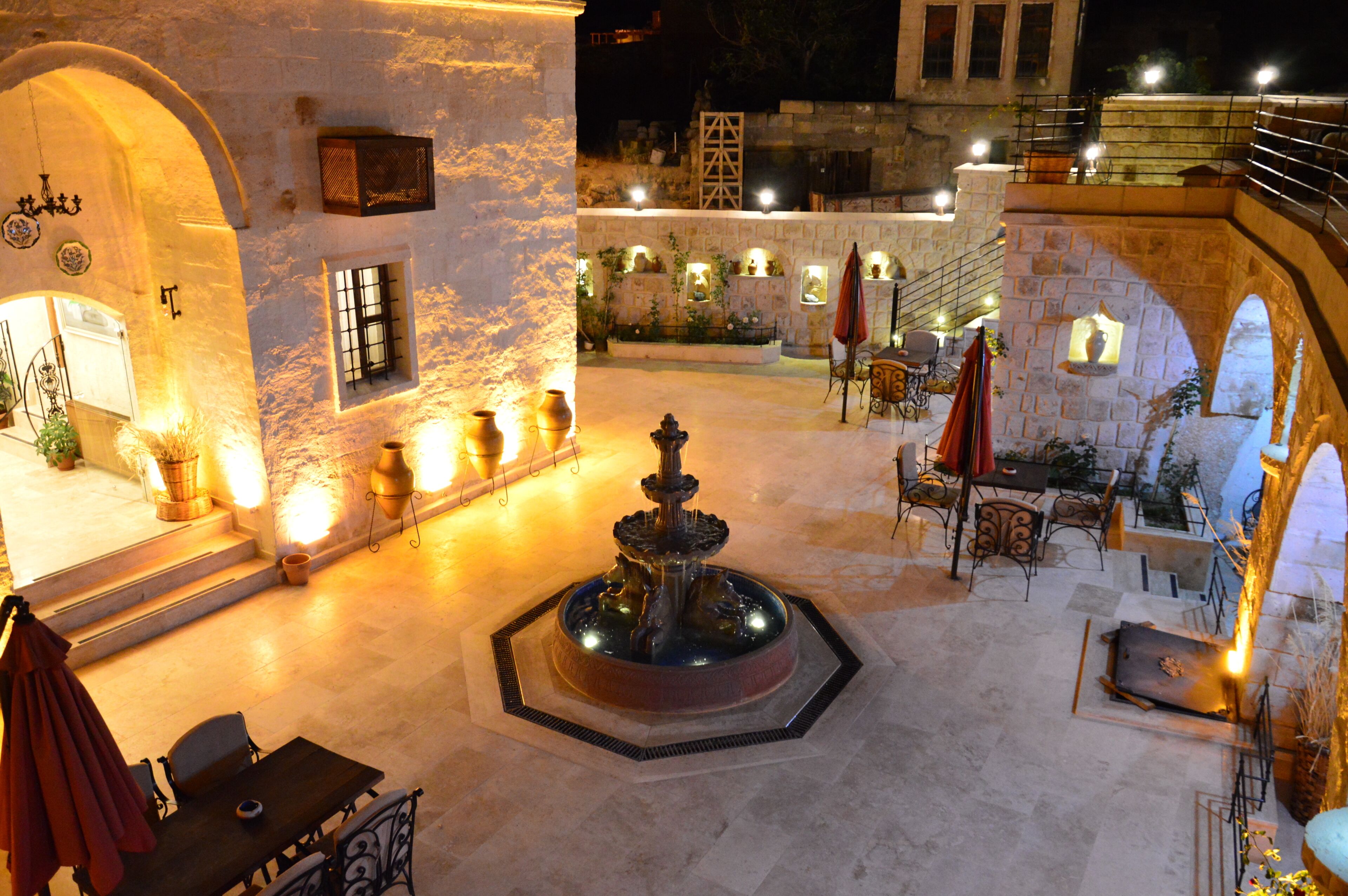 An outdoor courtyard with a fountain, stone walls, and outdoor seating.