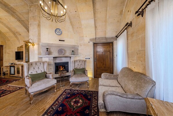 A spacious living room with a fireplace, two armchairs, a sofa, and a large rug. - Pegas Cave Suites (Ürgüp)