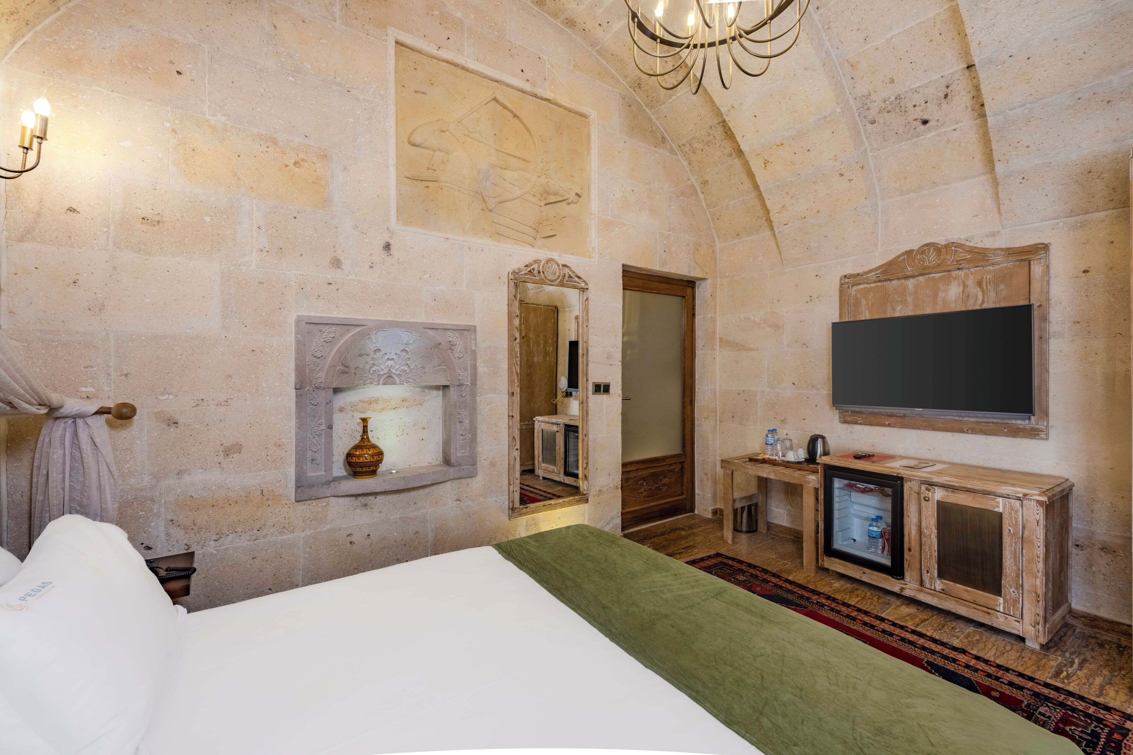 A stone-walled room with a bed, a fireplace, a television, and a mirror.