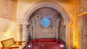 A stone-walled room with a circular stained glass window, a red carpeted area, and a bench. - Pegas Cave Suites (Ürgüp)