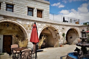 A stone building with arched doorways, outdoor seating with tables and chairs, and a fountain. - Pegas Cave Suites (Ürgüp)