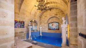 A stone-walled room with a blue-tiled pool, a bed, and a chandelier. - Pegas Cave Suites (Ürgüp)