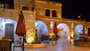 An outdoor courtyard with stone walls, arched doorways, and tables with chairs. - Pegas Cave Suites (Ürgüp)
