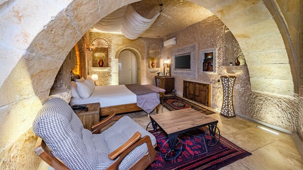 An arched stone room with a bed, a wooden table, a chair, and a TV. - Pegas Cave Suites (Ürgüp)