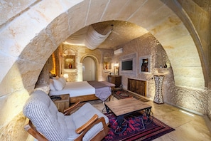 An arched stone room with a bed, a wooden table, a chair, and a TV. - Pegas Cave Suites (Ürgüp)