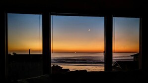A room with a large window overlooking a beach at sunset. - Experience Spacious Coastal Living at Seascape - Stunning Views of Heceta Beach  (Florence)