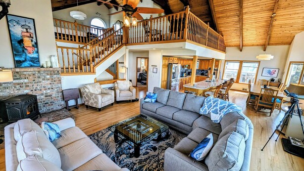 A spacious living area with a high ceiling, a fireplace, a staircase, and a kitchen visible in the background. - Experience Spacious Coastal Living at Seascape - Stunning Views of Heceta Beach  (Florence)
