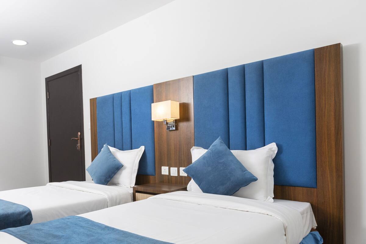 Habitación de hotel con dos camas, un armario de madera, un espejo y una lámpara fijada a la pared.