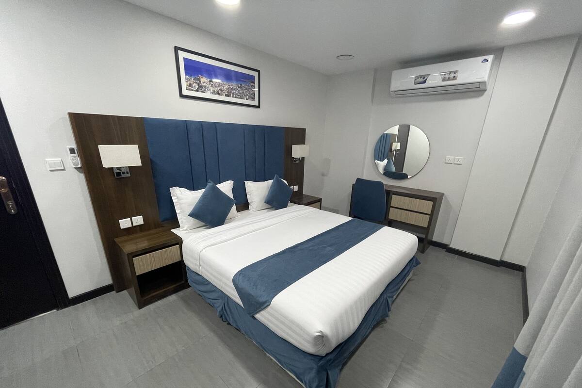 Una habitación de hotel moderna con una cama grande, cabecera, mesita de noche, espejo y equipo de aire acondicionado.