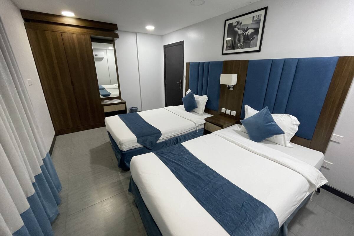 Habitación de hotel con dos camas, un armario de madera, un espejo, una mesita de noche y un aplique de pared.