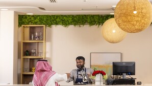 A reception area with a wooden shelf, a desk, a computer, and a decorative vase with red flowers. - Terrace View 1 serviced apartments - اطلالة الشرفة 1 للشقق المخدومة (Al Khobar)