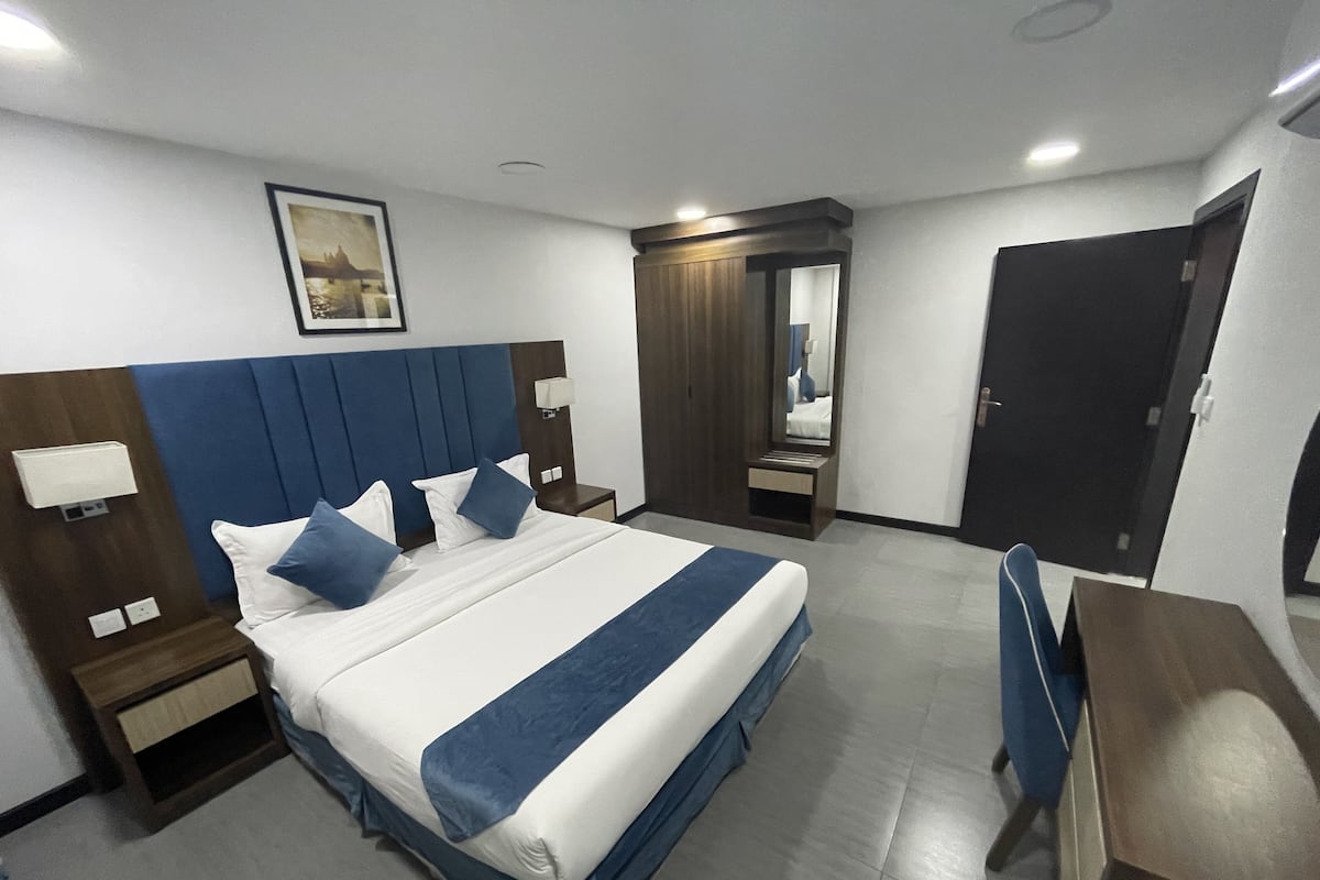 Una habitación de hotel con una cama grande, un escritorio, una silla, una mesita de noche, un espejo y una puerta.