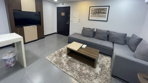 A modern living room with a grey sofa, a flat-screen TV mounted on a wooden cabinet, a small wooden coffee table, and a fluffy rug. - Terrace View 1 serviced apartments - اطلالة الشرفة 1 للشقق المخدومة (Al Khobar)