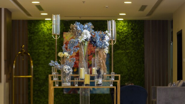 A reception area with a glass display of flowers and candles, a gold-framed desk, and a green wall in the background. - Terrace View 1 serviced apartments - اطلالة الشرفة 1 للشقق المخدومة (Al Khobar)